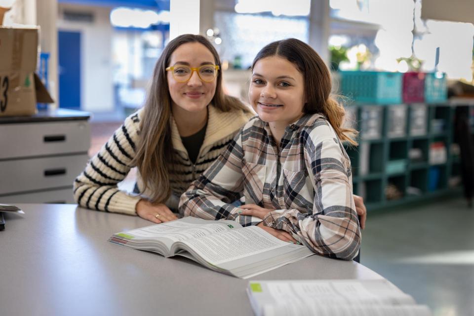 Teacher and middle school student sitting at desk and smiling. Table in front of them has an open book.